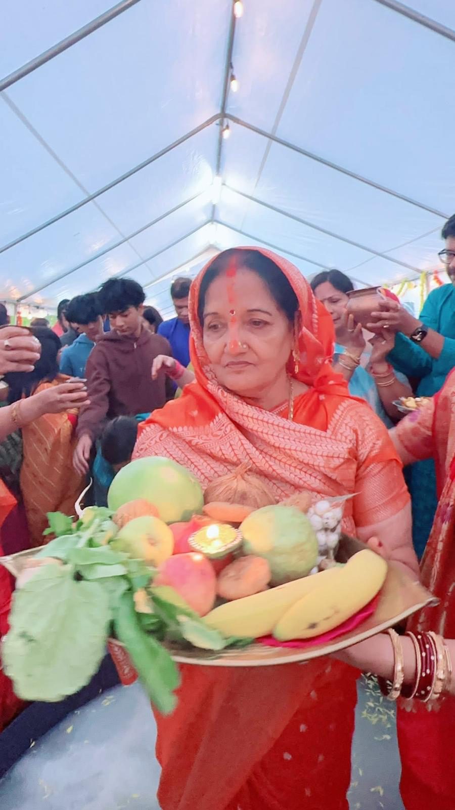 A Vrati in an orange saree carrying a soop heaped with fruit, sugarcane and a lit diya